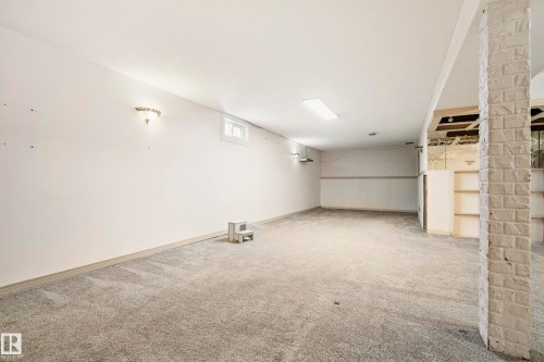 Spacious lower-level room featuring light gray carpeting, recessed lighting, wall sconces, a window, and a brick-textured support pillar - 14916 114A Street, Edmonton, AB 