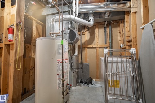 Utility area featuring a water heater, furnace system, exposed timber framing, and concrete flooring - 14916 114A Street, Edmonton, AB 