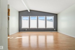 Spacious room featuring wood-finish flooring, a vaulted ceiling with an exposed beam, and a feature wall with four windows - 