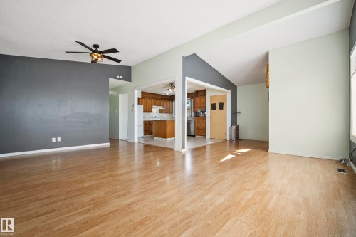 Open-concept living area featuring wood-finish flooring, vaulted ceilings, a ceiling fan with integrated lighting, and a partial view of the kitchen with wood cabinetry - 14916 114A Street, Edmonton, AB 