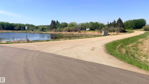 Paved road frontage with a gravel access road, bordered by a natural water feature and mature trees - 458 20212 Twp Road 510, Rural Strathcona County, AB 