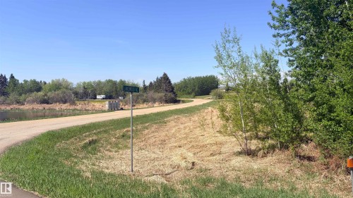 Gravel road frontage bordering a body of water, with mature trees and green space surrounding the property - 458 20212 Twp Road 510, Rural Strathcona County, AB 