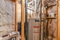 Water heater in a utility space with exposed wood framing, white insulation, and various pipes and ducts - 