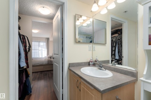 Ensuite bathroom featuring a textured ceiling, vanity, a spacious closet, and dark wood-style floors - 317 11441 Ellerslie Road, Edmonton, AB 
