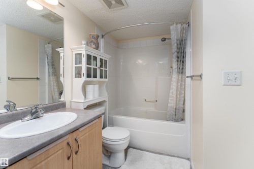 Bathroom with vanity, a textured ceiling, and shower / bathtub combination with curtain - 317 11441 Ellerslie Road, Edmonton, AB 
