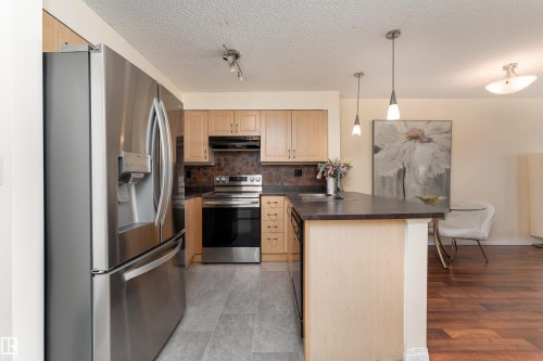 Kitchen with stainless steel appliances, dark countertops, a peninsula, decorative light fixtures, and backsplash - 317 11441 Ellerslie Road, Edmonton, AB 