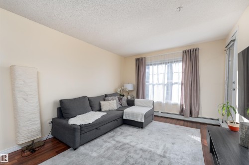 Living room with dark wood-style flooring, baseboard heating, and a textured ceiling - 317 11441 Ellerslie Road, Edmonton, AB 