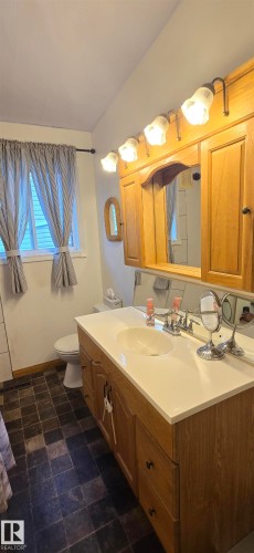 Bathroom vanity with a white countertop and integrated sink, complemented by a wood-finish cabinet and four drawers - 5304 49 Street, Two Hills, AB - Indoor Photo Showing Bathroom