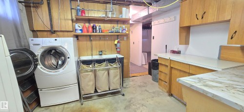 Functional utility space featuring a front-loading washer, wood-paneled walls, built-in shelving, and light wood cabinetry with a white countertop - 5304 49 Street, Two Hills, AB - Indoor Photo Showing Laundry Room