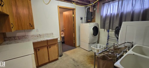 Utility area featuring wood cabinetry, a white countertop, and a double-basin utility sink - 5304 49 Street, Two Hills, AB - Indoor Photo Showing Laundry Room