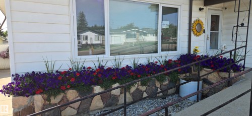 Front exterior featuring horizontal siding and a stone-clad planter with vibrant plantings - 5304 49 Street, Two Hills, AB - Outdoor With Exterior