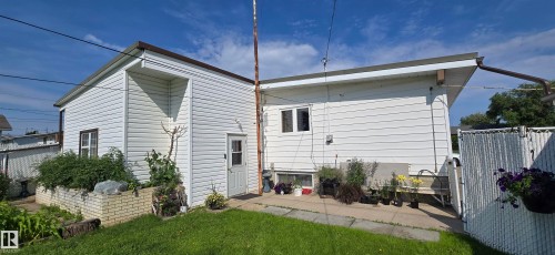 Rear exterior featuring white horizontal siding, a private patio, a low-profile brick retaining wall, and a fenced perimeter - 5304 49 Street, Two Hills, AB - Outdoor