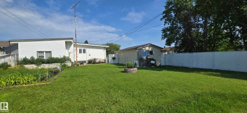 Expansive fenced backyard featuring a substantial lawn area, a built-in fire pit, and a garden bed - 5304 49 Street, Two Hills, AB - Outdoor