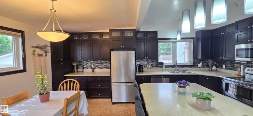 Kitchen featuring dark wood cabinetry, stainless steel appliances, a light-toned island countertop, and a mosaic tile backsplash - 5304 49 Street, Two Hills, AB - Indoor