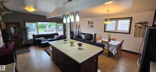 Spacious open-concept living area featuring an expansive central island with seating, pendant lighting, large windows, and durable wood-finish flooring - 5304 49 Street, Two Hills, AB - Indoor