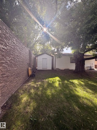 Enclosed rear yard featuring a privacy wall with stacked stone-look siding, a detached storage shed, and mature trees - 8 Savoy Place, St. Albert, AB 
