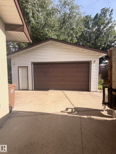 Detached garage featuring white vinyl siding, a brown panel garage door, a pedestrian door, and a concrete driveway - 8 Savoy Place, St. Albert, AB 
