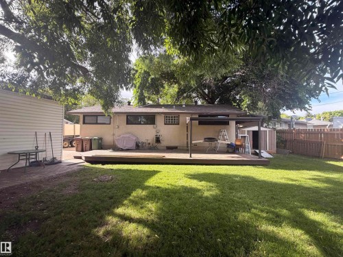 Spacious backyard featuring a large wood-finish deck with an attached patio cover, a manicured lawn, and mature trees providing natural shade - 8 Savoy Place, St. Albert, AB 