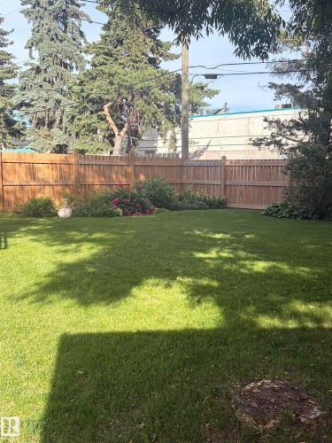 Expansive lawn area featuring a wood privacy fence, mature perimeter trees, and established garden beds with flowering shrubs - 8 Savoy Place, St. Albert, AB 