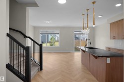 Open-concept living area featuring herringbone-pattern wood-finish flooring, a contemporary kitchen island with a dark countertop and integrated sink, and modern pendant lighting - 