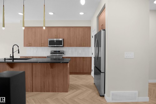 Kitchen featuring wood-finish cabinetry, stainless steel appliances, a center island with a dark countertop and integrated sink, white subway tile backsplash, and herringbone wood-finish flooring - 8523 Mayday Run, Edmonton, AB 