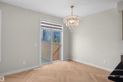 Bright room featuring a contemporary chandelier, wood-finish herringbone flooring, and a sliding glass door with privacy blinds providing access to the fenced outdoor area - 