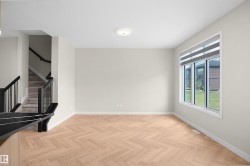 Open-concept living area with herringbone wood-finish flooring, a large window with roller shades, and a ceiling-mounted light fixture - 