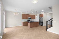 Open-concept living area with herringbone wood-finish flooring, a contemporary kitchen, stainless steel appliances, and a central island with pendant lighting - 