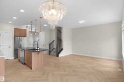Open concept living space featuring a contemporary chandelier, herringbone wood-finish flooring, a kitchen island with dark countertops, stainless steel appliances, and a modern staircase with dark railings - 