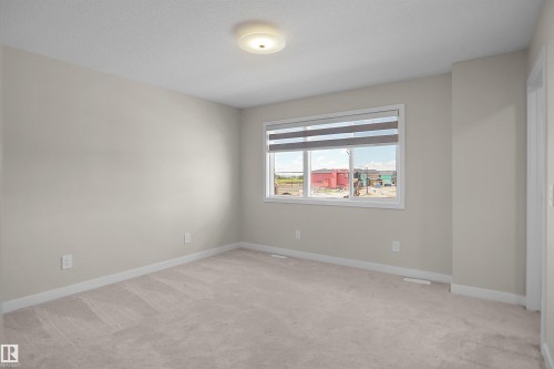 Carpeted room featuring a large window with horizontal blinds, neutral wall paint, and white trim - 8523 Mayday Run, Edmonton, AB 