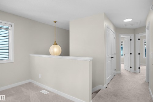 Upper-level hallway featuring neutral wall tones, light-colored carpet, white trim, and a contemporary pendant light fixture - 8523 Mayday Run, Edmonton, AB 