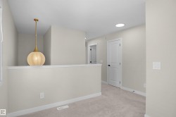 Upper-level landing featuring a contemporary pendant light fixture, recessed ceiling lighting, a white painted half-wall, neutral wall paint, and light-colored carpeting - 