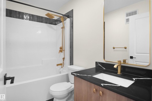 Modern bathroom featuring a vanity with a dark countertop and integrated white sink, golden-hued faucet, and a rectangular mirror with a golden-hued frame - 8523 Mayday Run, Edmonton, AB 
