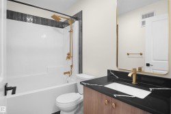 Modern bathroom featuring a vanity with a dark countertop and integrated white sink, golden-hued faucet, and a rectangular mirror with a golden-hued frame - 