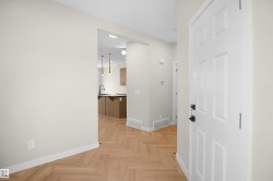 Entrance area featuring herringbone wood-finish flooring, white paneled door with black hardware, and light neutral wall paint - 