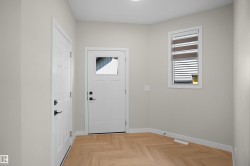 Entryway featuring wood-finish flooring in a herringbone pattern, two white paneled doors with matte black hardware, and a window with integrated blinds - 