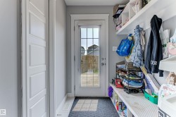 Entryway featuring a glass-paned door, built-in shelving, coat hooks, and a dark tile floor - 