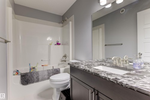Bathroom featuring a dark wood-finish vanity with an undermount sink, a stone-finish countertop, and a brushed nickel faucet - 1311 30 Avenue, Edmonton, AB 