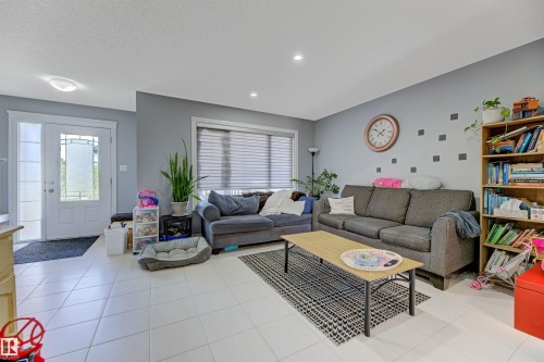 Bright living area featuring light-toned tile flooring, recessed lighting, and a front entry door with decorative glass inserts and a sidelight - 1311 30 Avenue, Edmonton, AB 