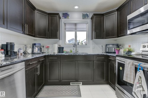 U-shaped kitchen featuring dark wood cabinetry, dark countertops, white tile flooring, and stainless steel appliances including a built-in microwave and dishwasher - 1311 30 Avenue, Edmonton, AB 