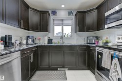 U-shaped kitchen featuring dark wood cabinetry, dark countertops, white tile flooring, and stainless steel appliances including a built-in microwave and dishwasher - 