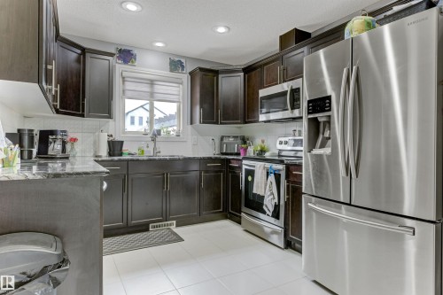 Kitchen featuring dark wood-finish cabinetry, stainless steel appliances, a window with blinds, recessed lighting, and light-toned tile flooring - 1311 30 Avenue, Edmonton, AB 