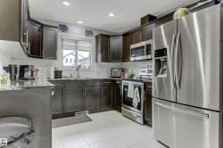 Kitchen featuring dark wood-finish cabinetry, stainless steel appliances, a window with blinds, recessed lighting, and light-toned tile flooring - 