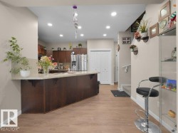 Kitchen featuring a large central island with seating, wood-finish flooring, recessed lighting, and a neutral color palette - 