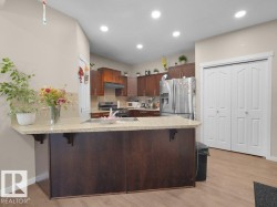 Kitchen featuring a central island with a light-toned countertop, wood-finish cabinetry, stainless steel appliances, recessed ceiling lighting, and light wood-finish flooring - 