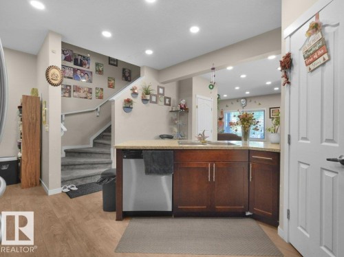 Kitchen peninsula featuring wood-finish cabinetry, light-toned countertop, and stainless steel dishwasher - 1419 27 Av, Edmonton, AB 