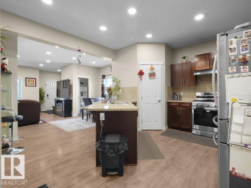 Kitchen featuring an island with a built-in sink, wood-finish flooring, recessed lighting, and stainless steel appliances including a refrigerator and range with overhead microwave - 1419 27 Av, Edmonton, AB 