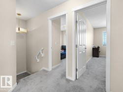 Upper-level hallway featuring neutral wall paint, light gray carpet, white trim, and a modern gold-tone ceiling fixture - 