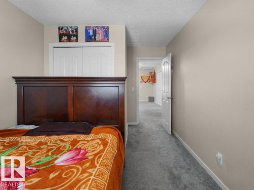 Bedroom featuring light-toned walls, gray carpeting, a dark wood-finish headboard, and bi-fold closet doors - 1419 27 Av, Edmonton, AB 