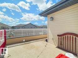 Spacious concrete patio featuring a white railing, beige siding, and an exterior wall light fixture - 